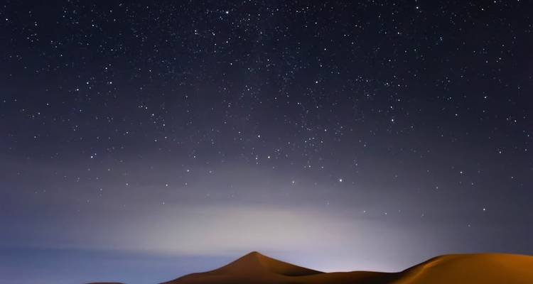 Ciel nocturne du désert étoilé au-dessus de dunes de sable doucement illuminées