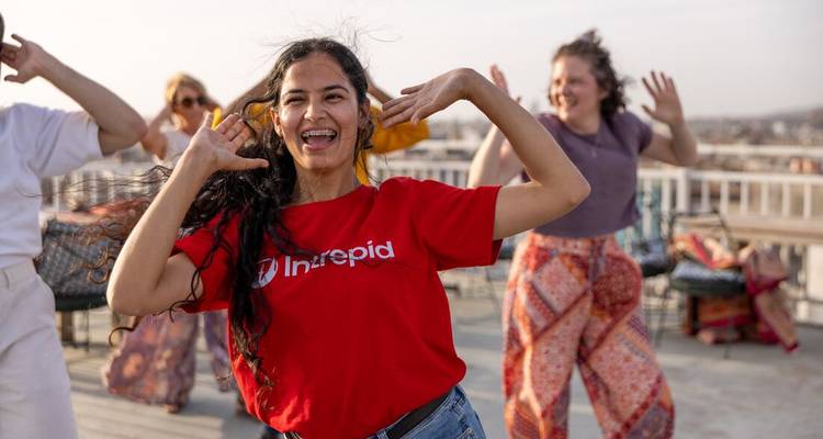 De jeunes voyageurs dansent et rient sur un toit, la femme qui les mène portant un t-shirt Intrepid.