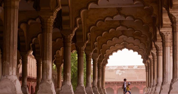 Deux visiteurs se promènent sous les grandes arches mogholes de l'arcade en grès du Fort d'Agra.