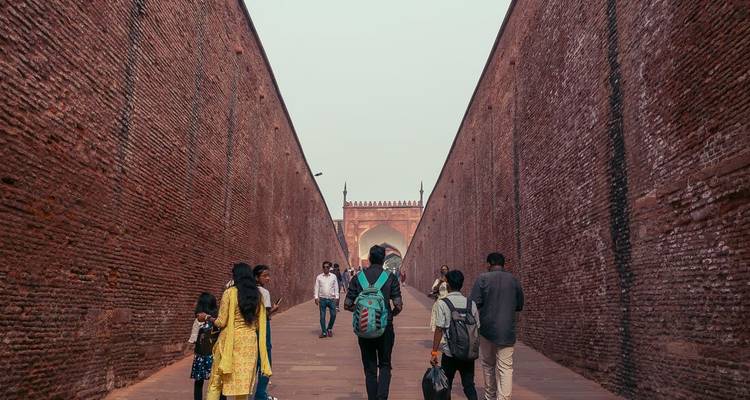 Les touristes marchent à travers un long passage étroit bordé de hauts murs de grès rouge vers une porte de fort.