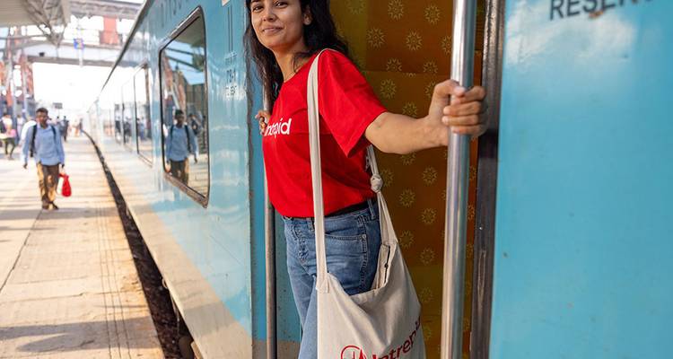 Une voyageuse sourit en montant dans un train longue distance bleu dans une gare.