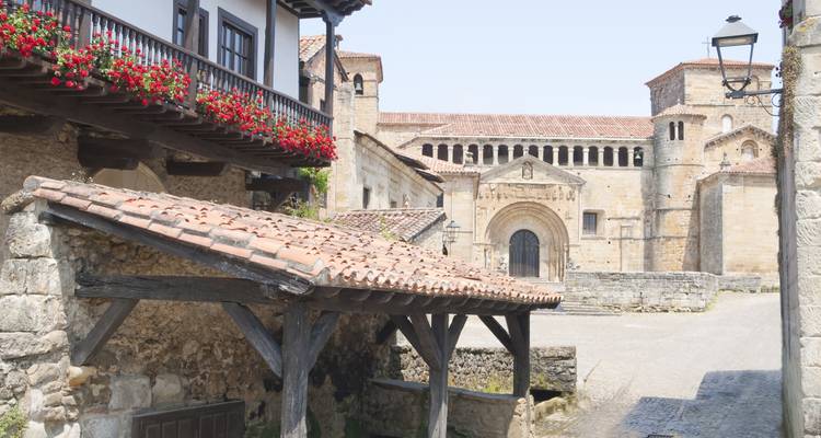 Rue pavée tranquille à Santillana del Mar avec balcon fleuri et église romane.