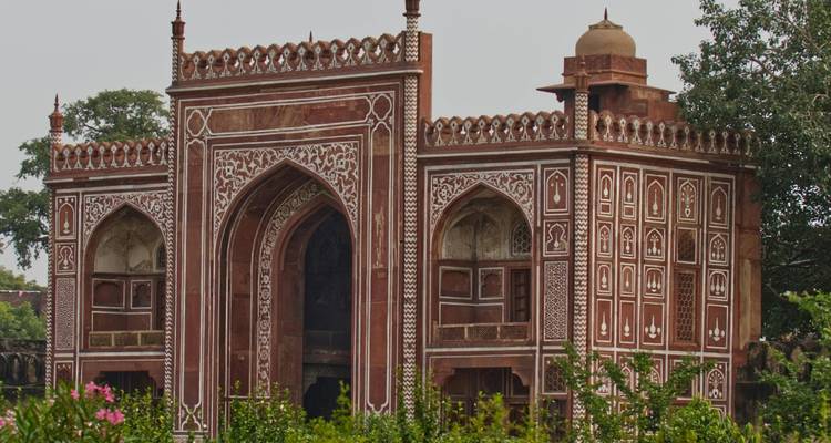 Een sierlijke Mughal-poort versierd met ingewikkelde witte inlegpatronen kijkt uit op een weelderige tuin.