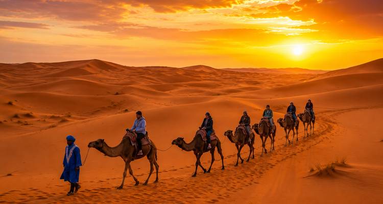 Kamelkarawane unter der Führung eines in blaues Gewand gekleideten Führers, die bei Sonnenuntergang über leuchtende Sahara-Dünen zieht.