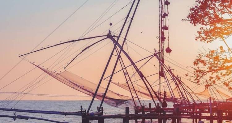 Silhouetted Chinese fishing nets extend over the Arabian Sea against a warm sunset sky