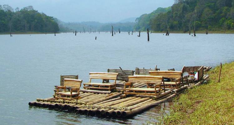 Hand-crafted bamboo raft with wooden chairs floats on a quiet lake surrounded by forested hills