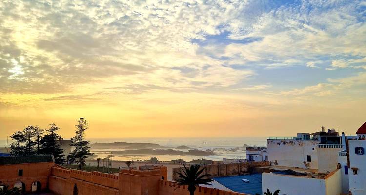 Sanfter goldener Sonnenaufgang über Essaouiras Stadtmauern und der Atlantikküste mit vereinzelten Wolken.