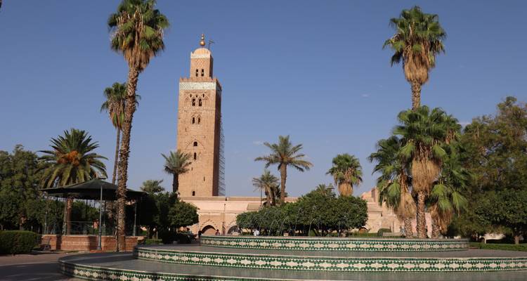 Das Minarett der Koutoubia-Moschee erhebt sich hinter einem gefliesten Brunnen und Palmen unter einem klaren blauen Himmel.