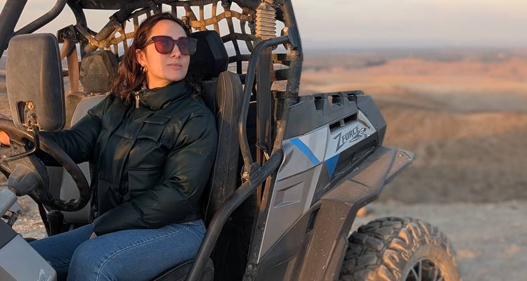 Frau mit Sonnenbrille fährt einen offenen Geländebuggy über ein sonnenbeschienenes Wüstenplateau.