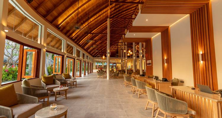 Spacious open-air resort lobby lined with wooden beams, comfy chairs and floor-to-ceiling windows.