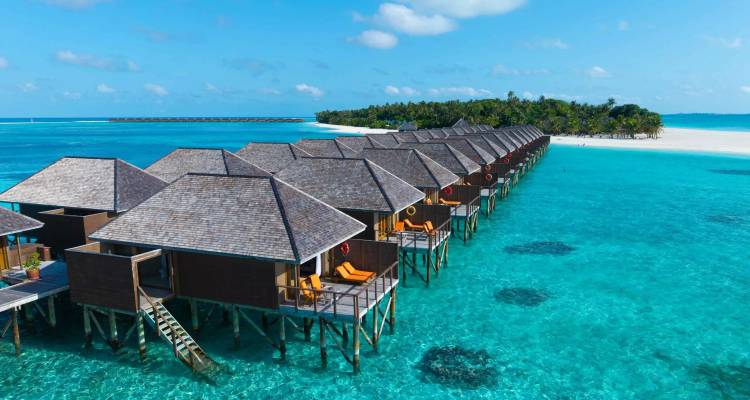 Row of over-water bungalows stretches into the turquoise lagoon with a palm-fringed island in the background.