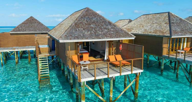 Close view of a wooden water-villa deck with loungers above clear azure water in the Maldives.