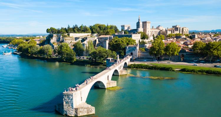 Pont de pierre médiéval emblématique enjambant une rivière verte menant à la cité fortifiée d'Avignon avec le Palais des Papes visible par une journée ensoleillée.