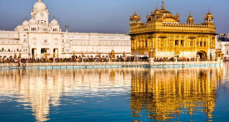 The Golden Temple and its shimmering reflection glow during early light while worshippers gather around the holy pool.