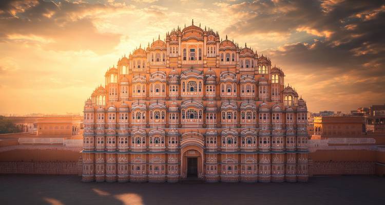 Facade ornementale en grès rose du palais Hawa Mahal brillant à la lumière douce du matin sous des nuages dramatiques.