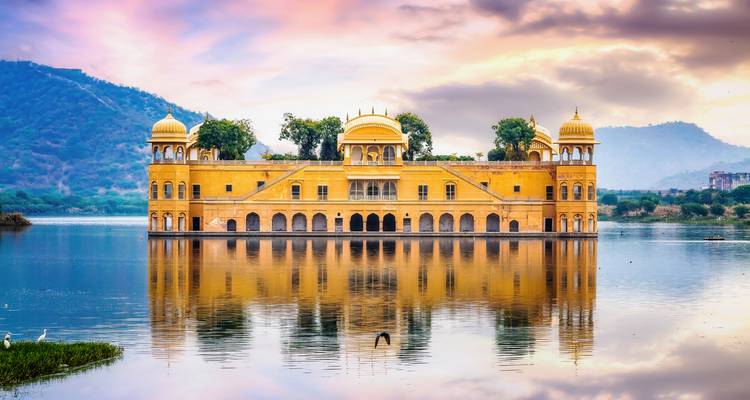 Le palais jaune de Jal Mahal se reflétant parfaitement dans un lac calme avec des collines lointaines sous un ciel coloré au lever du soleil.
