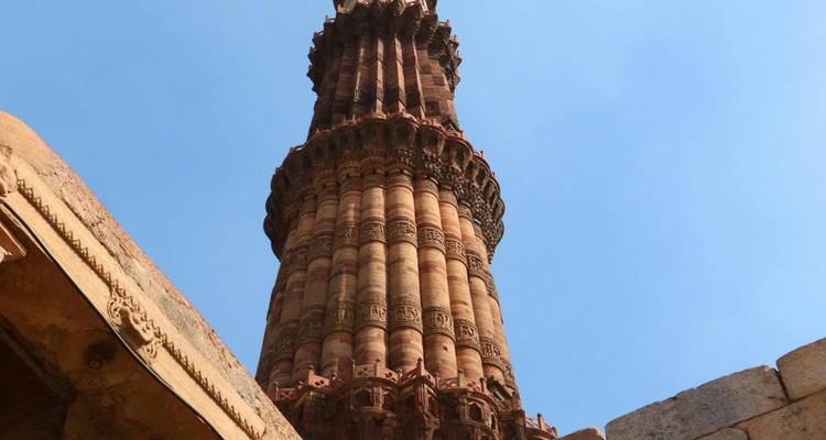 Vue en contre-plongée de la tour Qutub Minar en grès rouge finement ciselé sur un ciel bleu dégagé.