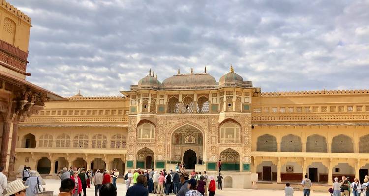 Crowds explore ornate Amber Fort courtyard with intricate gateway and cloudy sky overhead.