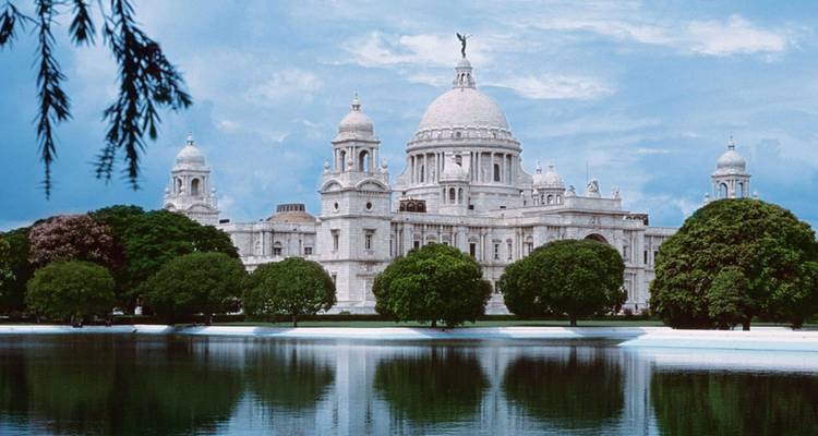 Groot wit Victoria Memorial weerspiegeld in een kalme vijver, omlijst door goed onderhouden bomen en een zachte bewolkte hemel.