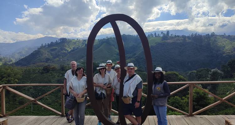 Groupe portant des chapeaux blancs posant sur une terrasse en bois surplombant des collines de café verdoyantes