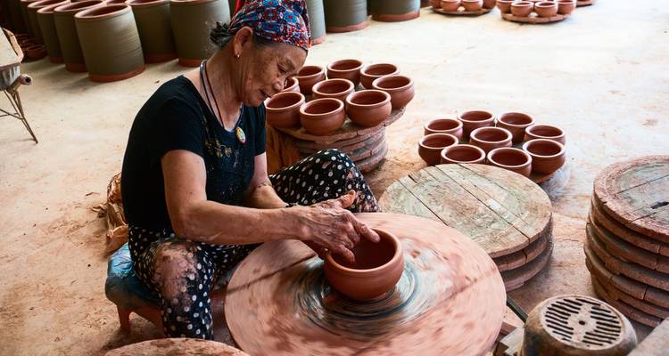 Un artesano da forma a una vasija de arcilla en un torno giratorio en un taller tradicional rodeado de cerámica terminada