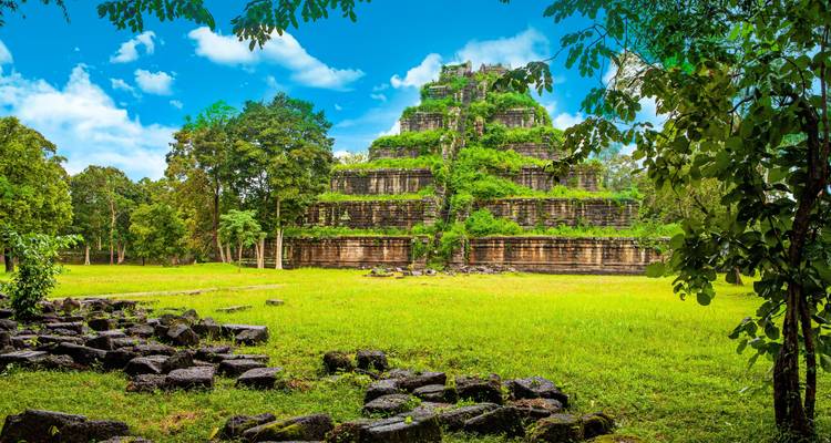 Templo piramidal de piedra cubierto de vegetación se eleva desde un claro verde brillante en la selva camboyana
