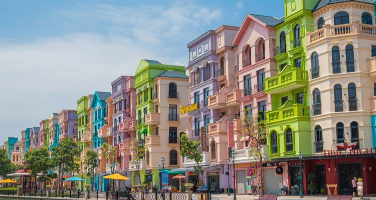 Reihe pastellfarbener Ladenfronten im europäischen Stil entlang einer sonnigen Fußgängerstraße mit Sonnenschirmen und Cafés