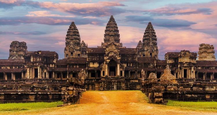 Ikonische Türme von Angkor Wat erheben sich gegen einen lebendigen rosa und violetten Abendhimmel über einem grasbewachsenen Damm