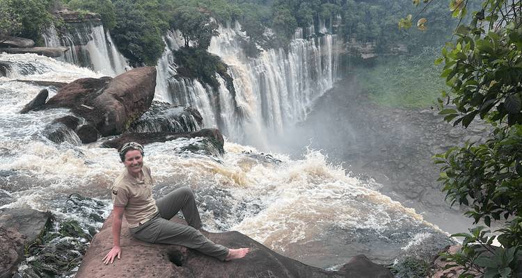 Voyageur assis pieds nus sur un rebord rocheux à côté d'une cascade rugissante entourée de jungle