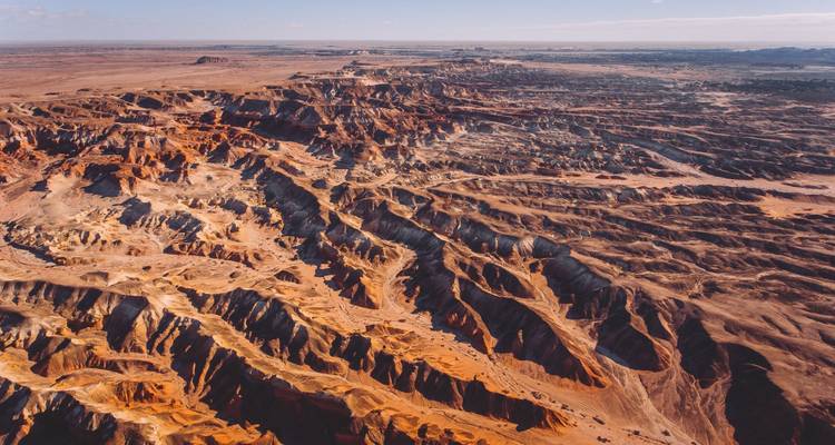 Vue aérienne de canyons désertiques accidentés rouge et gris s'étendant à l'horizon sous un ciel dégagé
