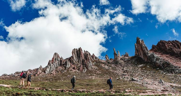 Hikers trek beneath jagged pink rock spires under a sky of billowing white clouds.