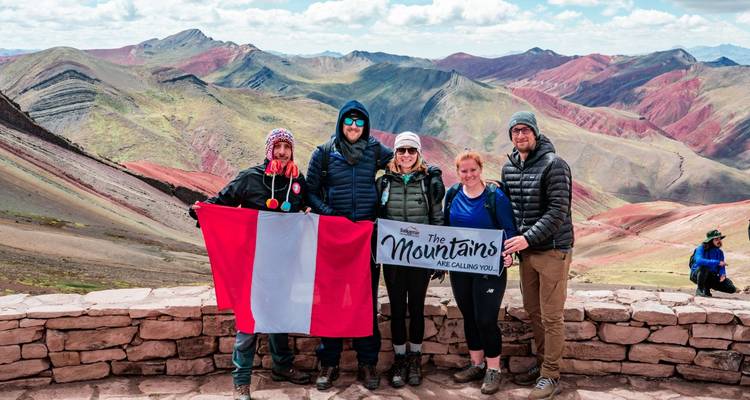 Group poses with Peruvian flag and banner at a spectacular Rainbow Mountain lookout.