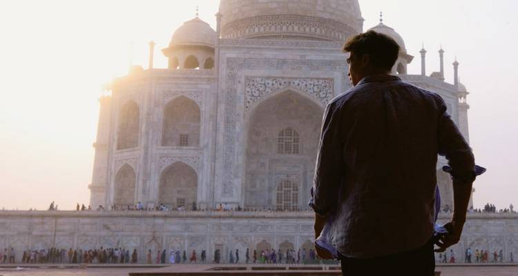 Silhouetted traveller gazes at the sun-lit marble facade of the Taj Mahal at dawn.