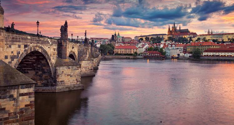 Prague’s Charles Bridge spanning the Vltava River at vibrant sunset with Prague Castle illuminated.