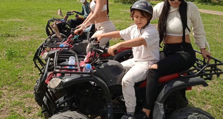 Une femme et deux enfants se préparent à faire de la motocross sur quad bikes dans un champ herbeux.
