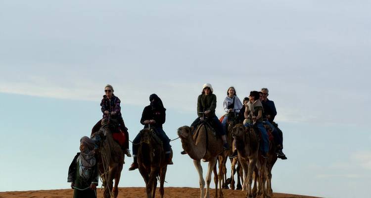 Des voyageurs chevauchant une file de chameaux le long de la crête d'une dune désertique sous un ciel ouvert.
