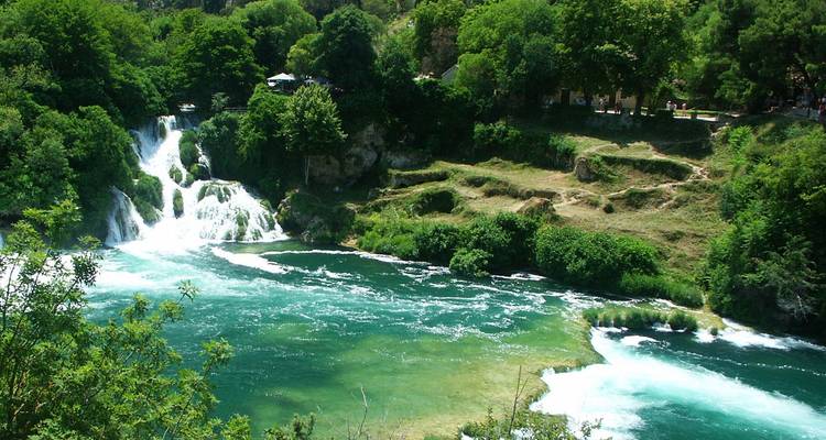 Der smaragdgrüne Fluss stürzt über mehrere üppige Wasserfälle ab, die von dichter Vegetation umrahmt sind.