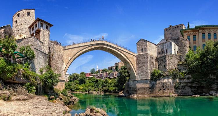 Ikonische gewölbte Steinbrücke über einen türkisfarbenen Fluss mit historischen Gebäuden an beiden Ufern.