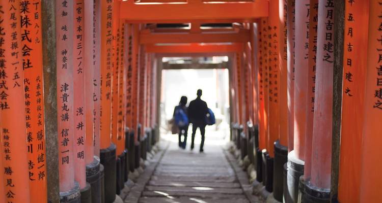 Los visitantes perfilados caminan a través del túnel de torii de color bermellón del Santuario Fushimi Inari.