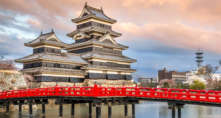 Les tours de bois sombre du château de Matsumoto s'élèvent au-dessus d'un pont rouge vif enjambant les douves immobiles à l'heure dorée.