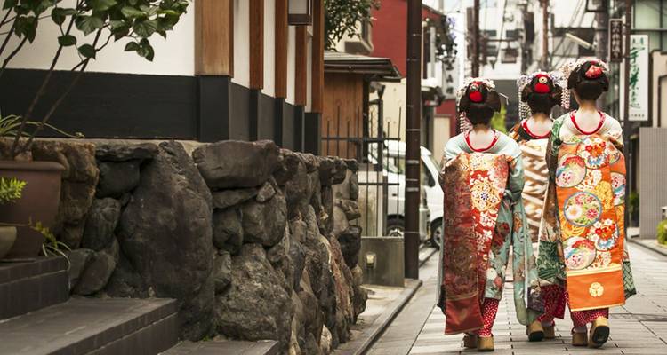 Drei Frauen in kunstvollen Kimonos, die eine enge historische Gasse in Kyoto hinuntergehen