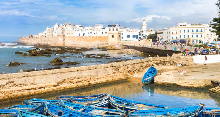 Sea walls and whitewashed medina of Essaouira with blue fishing boats in the foreground.