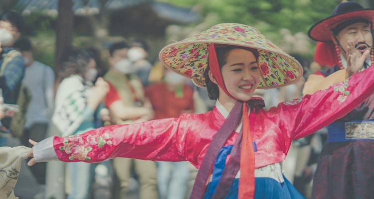 Mujer sonriente con un colorido hanbok realiza una danza tradicional al aire libre, con los brazos bien abiertos.