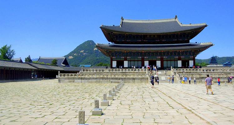 Bezoekers verkennen de grote binnenplaats van Gyeongbokgung Palace met bergen op de achtergrond onder een hemelsblauw