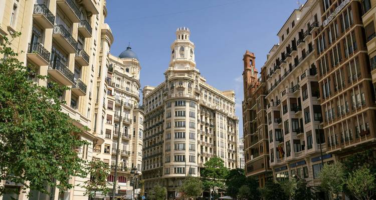 Elegante gebouwen uit het begin van de 20e eeuw langs een groene straat in het centrum van Valencia onder een heldere hemel.