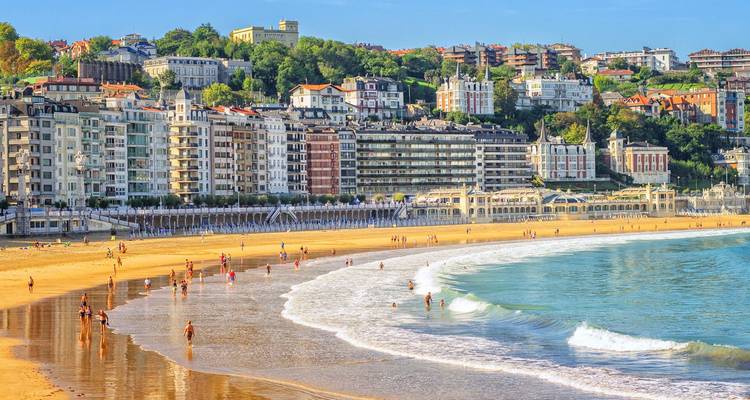 Curving golden sands of La Concha beach lined with elegant buildings and sunbathers under clear skies.