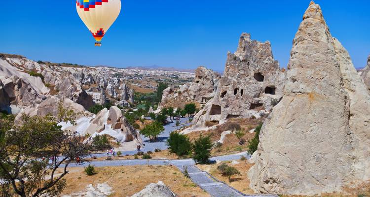 Fairy-chimney rock formations in Cappadocia with a colorful hot-air balloon above.