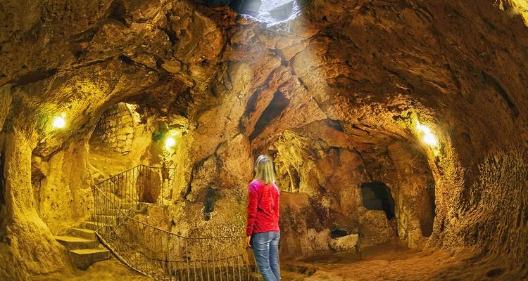 Visitor gazes up at illuminated volcanic rock walls inside an underground city cave in Cappadocia.