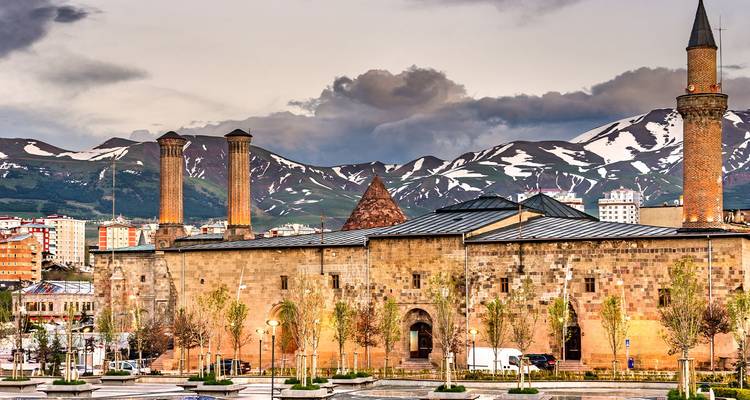 Doppelminarett-Steinmedrese in Erzurum vor schneebedeckten Bergen und dramatischem Himmel