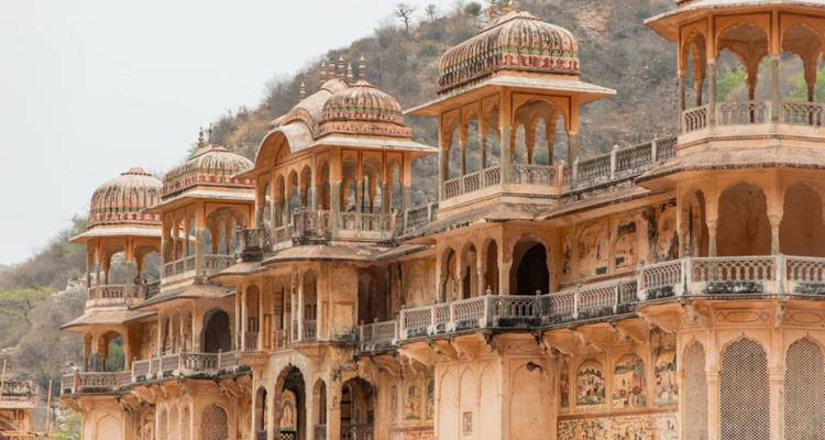 Series of ornate sandstone cenotaphs with domes and arches set against hillside in Rajasthan.